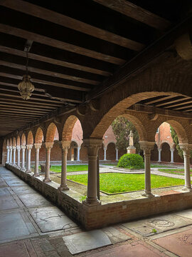 Beautiful historic cloister courtyard in Venice featuring elegant arches, stone columns, and a peaceful garden with a statue in the center. Classic European architecture with symmetry and calm atmosph
