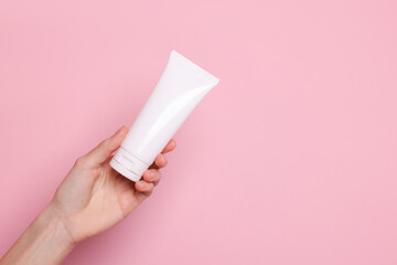 Fototapeta premium Woman holding tube of hand cream on pink background, closeup. Space for text