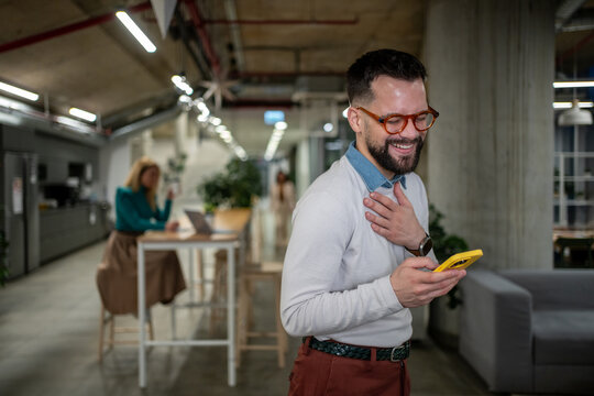Happy man laughing while using smartphone in office