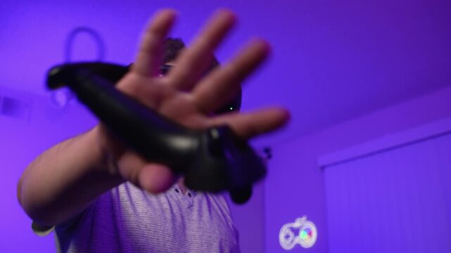 Man in VR headset reaching hand forward interacting with virtual object performing gestures and immersing into digital environment with presence effect in room with neon lighting