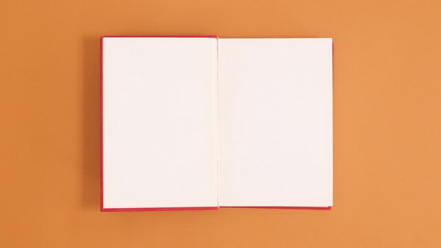 Top view of an open notebook with blank white pages on an orange background, perfect for writing notes or creative ideas.