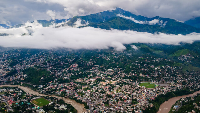 Aerial view of the urban landscape of Muzaffarabad city nestled in a valley with a winding river and surrounded by green mountains under low clouds Muzaffarabad, Azad Kashmir, Pakistan.