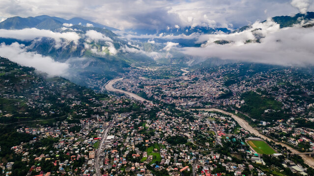 Aerial view of the sprawling city buildings nestled in a deep mountain valley with a winding river under low clouds Muzaffarabad, Azad Kashmir, Pakistan.