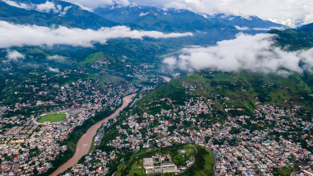 Aerial view of the urban landscape of Muzaffarabad nestled in a mountain valley with a winding river and low-hanging clouds Muzaffarabad, Azad Kashmir, Pakistan.