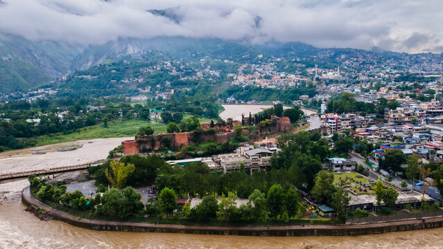 Aerial view of the historic Red Fort surrounded by lush trees and the winding river with the city and cloudy mountains in the background Muzaffarabad, Azad Kashmir, Pakistan.