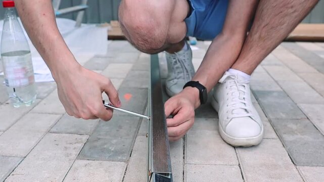 One installer uses a screwdriver to attach a screw to a metal shed piece.