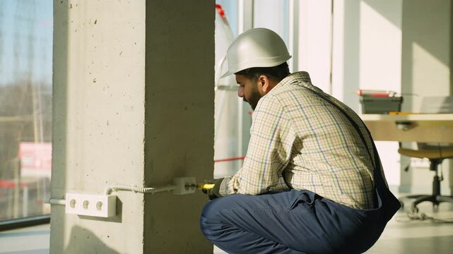 Professional electrician installing wall socket on construction site