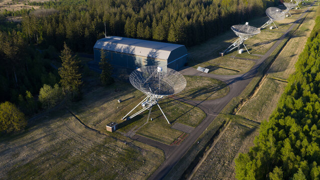 Aerial view of the Westerbork Synthesis Radio Telescope dishes and a large hangar building surrounded by dense green forest and open fields Zwiggelte, Drenthe, Netherlands.