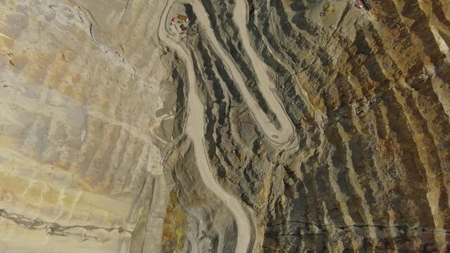 Aerial tilt view of open pit copper ore mine and heavy mining equipment. Excavator and mining trucks in quarry, 4k