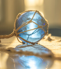 Artistic macro of blue glass fishing float with rope net casting reflection on glossy surface in dramatic light. © Trygve