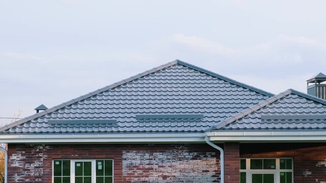 Close-up of modern house roof with gray metal tiles and brick facade with efflorescence stains, partial view, suburban residential property and construction quality concept
