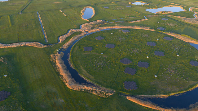 Aerial view of the LOFAR superterp radio telescope station with its circular island and antenna arrays surrounded by lush green fields and water channels Buinen, Drenthe, Netherlands.