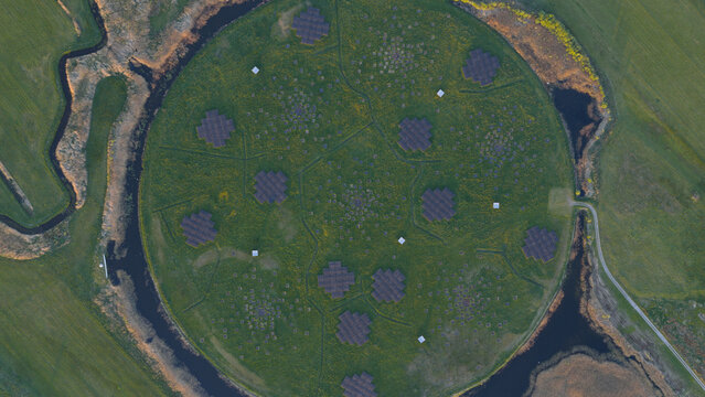 Aerial view of the LOFAR superterp radio telescope station with its circular green mound and geometric antenna arrays surrounded by water channels in Buinen, Drenthe, Netherlands.