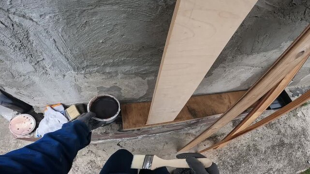 Worker dips brush into bucket of dark wood varnish. First person view. Concept of repair, construction or DIY project. Repair and protection of wood. Woman doing renovation or redesign