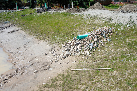 New industrial plastic pipe sticking out of a dirt hillside, onto rocks to prevent erosion, for stormwater to spill into a water retention pond
