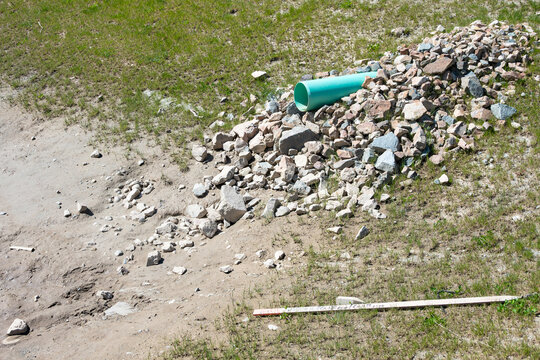 New industrial plastic pipe sticking out of a dirt hillside, onto rocks to prevent erosion, for stormwater to spill into a water retention pond
