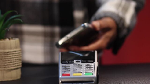 Customer using smartphone for contactless payment on a pos terminal. Nfc technology allowing for secure, fast, and easy tap to pay transactions in a retail store or cafe