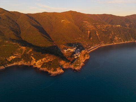 Aerial view of the historic village of Corniglia perched on a rocky cliff overlooking the Mediterranean Sea during golden hour with lush green mountains in the background Corniglia, Liguria, Italy.
