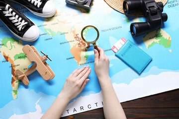 Naklejka premium Woman with magnifying glass and world map planning trip at wooden table, top view