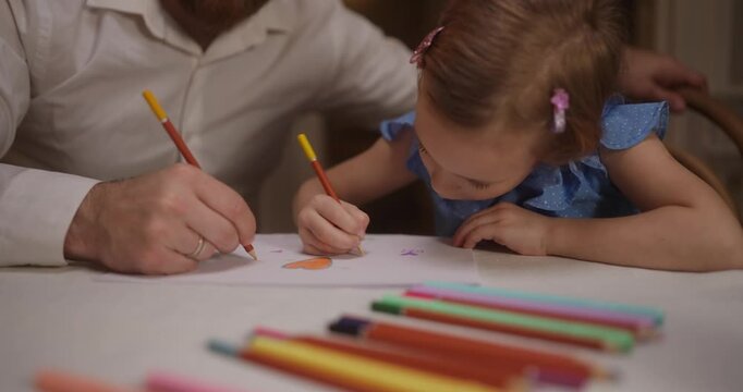 A child joyfully draws with bright markers beside a caring parent, sharing a special creative moment