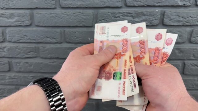 Man counts red paper 5000 rubles bills. Russian cash money in male hand. A man holds a wad of money in his hands. A close-up of a man's hands counts a bundle of bills for five thousand Russian rubles.