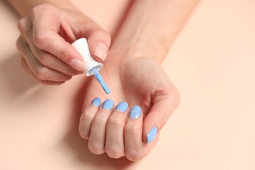 Woman applying blue nail polish onto her nails at beige table, closeup