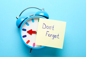 Obraz premium Reminder. Alarm clock and sticky note with phrase Don't forget on light blue background, top view