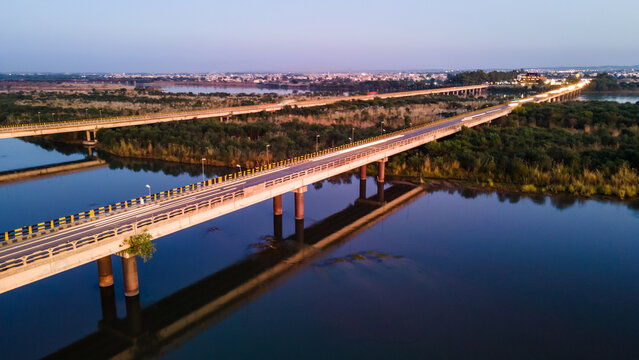 Aerial view of the long Jhelum Bridge spanning across the Jhelum River with lush green banks and the city skyline under a soft twilight sky Jhelum, Punjab, Pakistan.