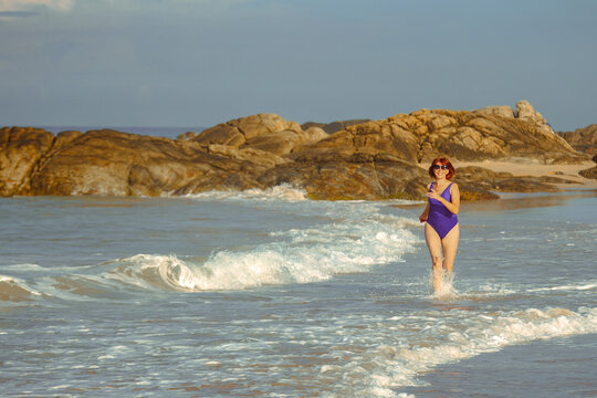 Woman in purple swimsuit running in ocean waves on a rocky beach