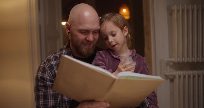 Father and daughter share a magical bedtime moment, reading a storybook together in a warm, inviting atmosphere