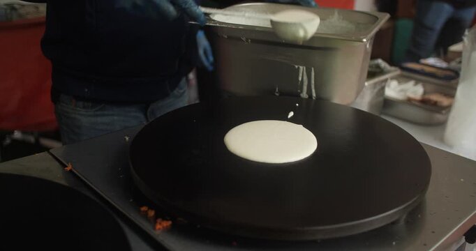 Chef spoons pancake mix onto hot plate Indian Dosa Roti street food snack
