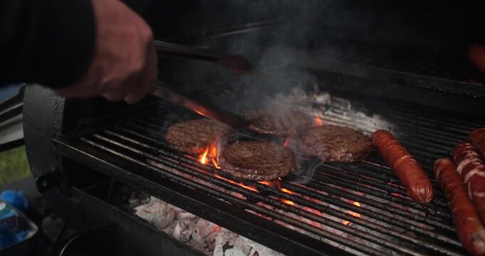 Summer barbecue BBQ cook flips flame grilled burger and hot dog sausages