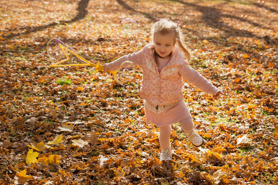 Cute little girl playing with soap bubbles and leaves in the fall forest. Happy child girl laughing in the autumn park. Kid and autumn season concept. Selective focus