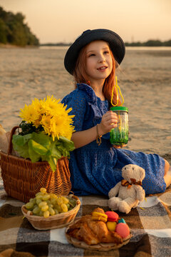 Beautiful little smiling girl sits with the lemonade front of the river bank. Little child girl on the family picnic on the nature. Kid and child on vacation. Selective focus.