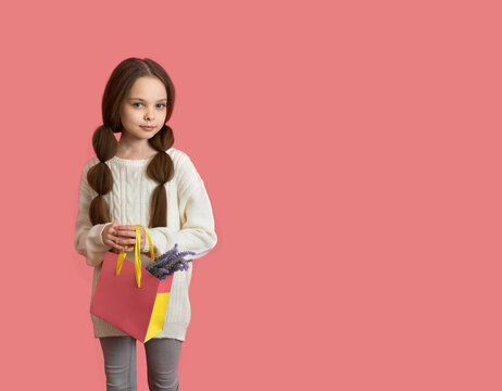 Cute little child girl with long hair holds a pink paper bag with lavender flower. Kid and celebration of 
holidays. Little girl shopping.