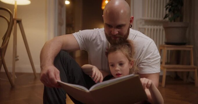 A father and daughter share a joyful moment exploring a colorful storybook in their cozy home