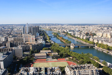 Obraz premium Aerial view of Paris with the Seine river, bridges and urban architecture. Scenic cityscape with residential buildings, parks and infrastructure under clear blue sky.