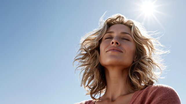Woman enjoying warm sun and fresh air outdoors, eyes closed in peaceful contentment, feeling carefree and healthy against a clear blue sky, experiencing well being, freedom, and vitality