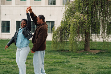 Fototapeta premium Happy african american couple dancing together in a park. Man and woman enjoying a relaxed day out, sharing happiness