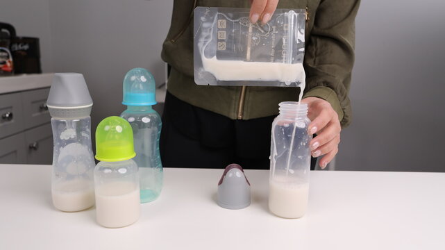 Person pouring stored breast milk from a plastic storage bag into a baby bottle, preparation for infant feeding.