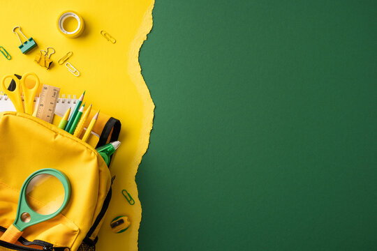 Back to school yellow backpack filled with supplies on torn green paper background for layout