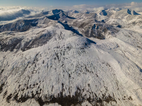 Aerial view of the snow-covered peaks and rugged ridges of Babusar Pass under a bright sky with soft clouds Babusar, KPK, Pakistan.