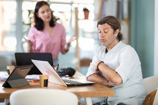 Aggressive female manager yelling and gesturing at upset man sitting at computer in workplace