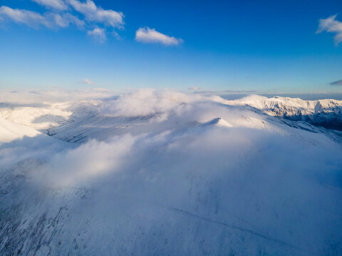 Aerial view of Babusar Pass covered in snow with thick clouds rolling over the mountain peaks under a blue sky Babusar, KPK, Pakistan.