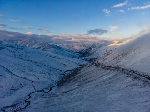 Aerial view of Babusar Pass with snow-covered mountain peaks, a winding road, and a frozen river valley under a clear blue sky in Babusar, KPK, Pakistan.