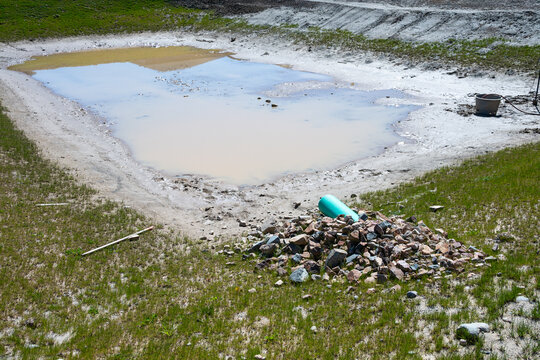 New industrial plastic pipe sticking out of a dirt hillside, onto rocks to prevent erosion, for stormwater to spill into a water retention pond
