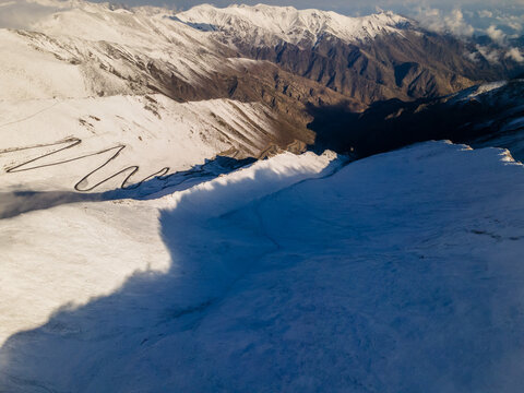 Aerial view of the winding road of Babusar Pass through snow-covered mountain peaks under bright sunlight in Babusar, KPK, Pakistan.