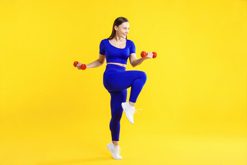 Fototapeta premium Woman in sportswear with dumbbells on yellow background
