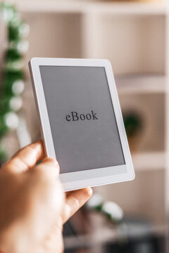 Stylish hand holding slim ebook reader in bright modern room. Clean aesthetic scene with simple technology, digital lifestyle and comfortable access to books, news and personal growth content.