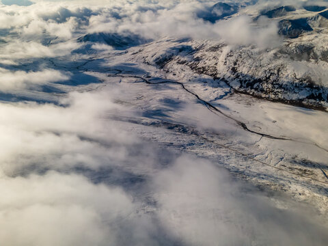 Aerial view of the snow-covered Babusar Pass with a winding road through mountain peaks and thick white clouds in Babusar, KPK, Pakistan.